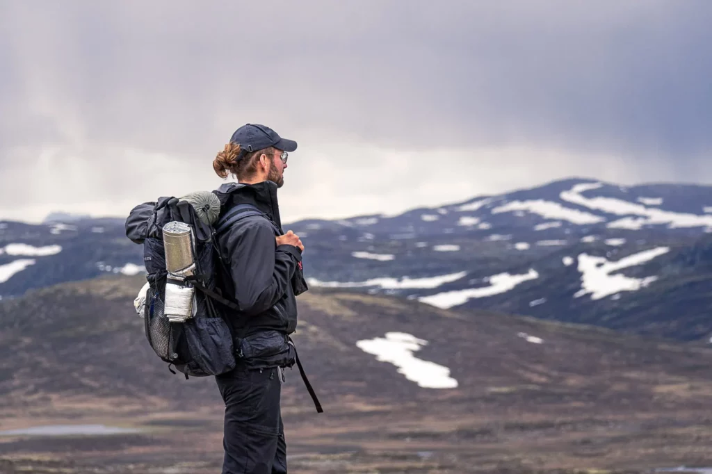 Wanderer mit Rucksack steht vor karger Landschaft