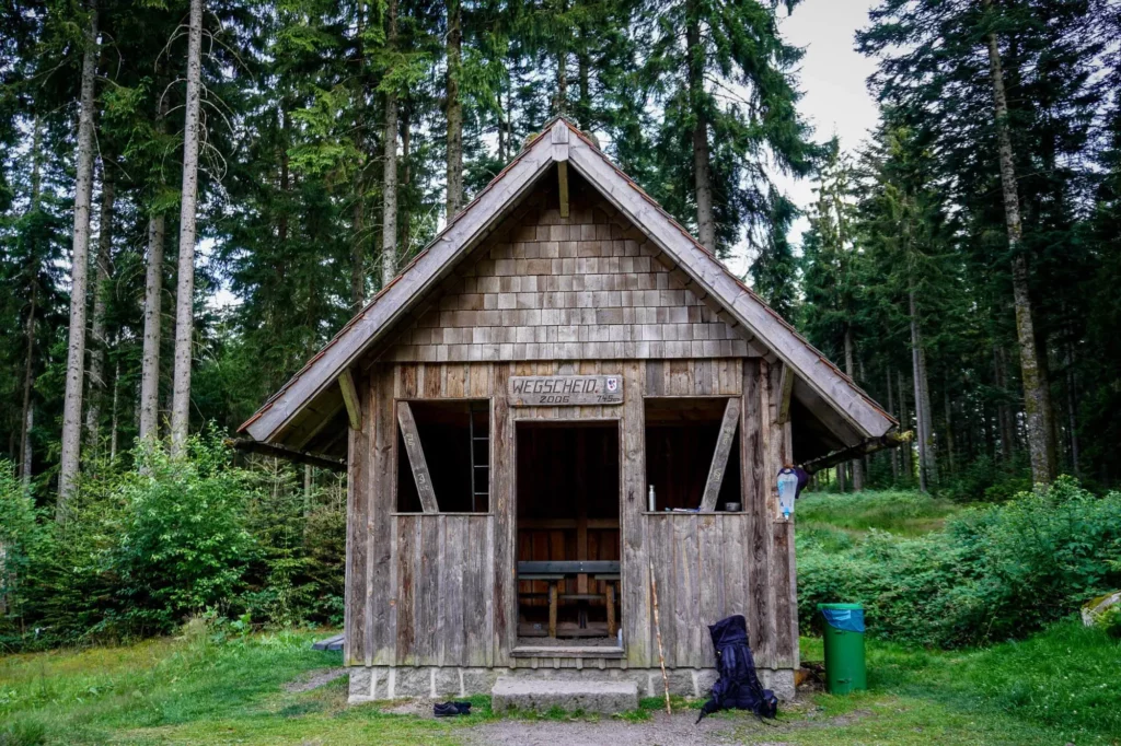 Holzhütte im Wald mit Wanderrucksack davor auf Deutschlandwanderung E1