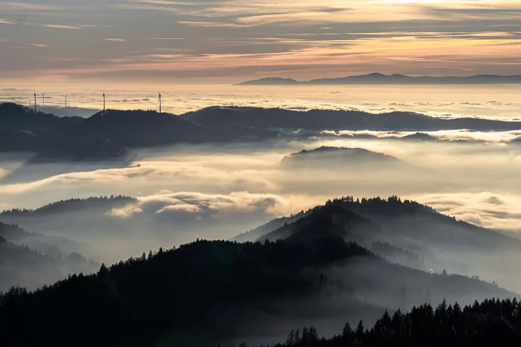Aussicht von oben auf Nebel zwischen Bergen und Windrädern im Hintergrund