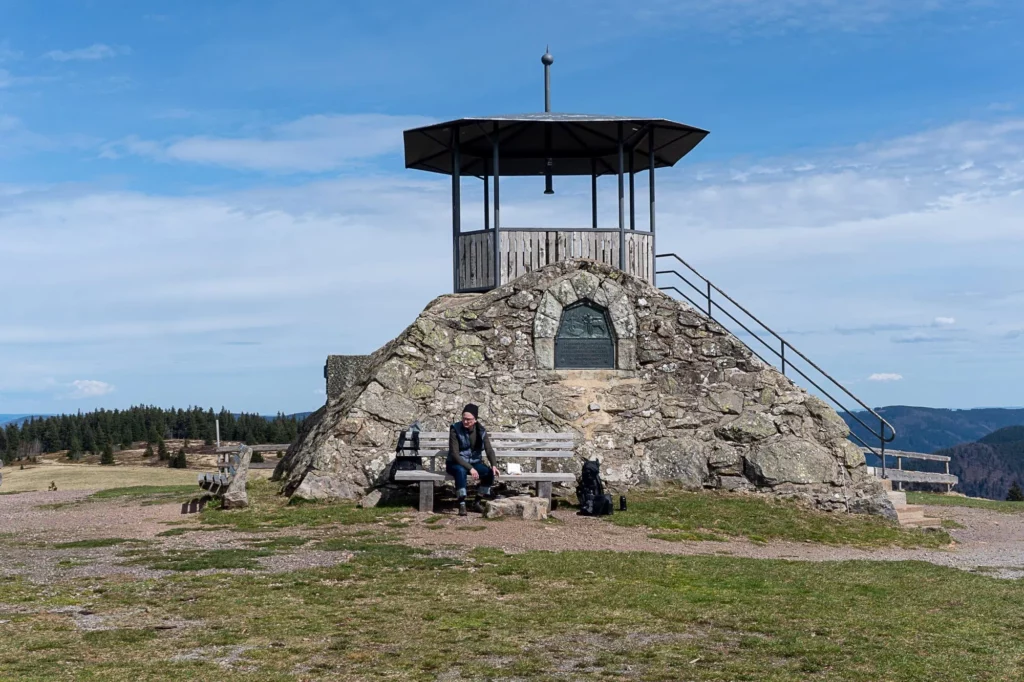 Wanderer sitzt auf Bank an einem Steingebilde