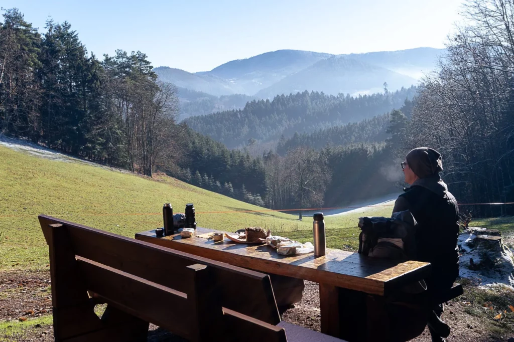Wanderer sitzt auf Bank mit gedecktem Tisch und schaut in die Ferne