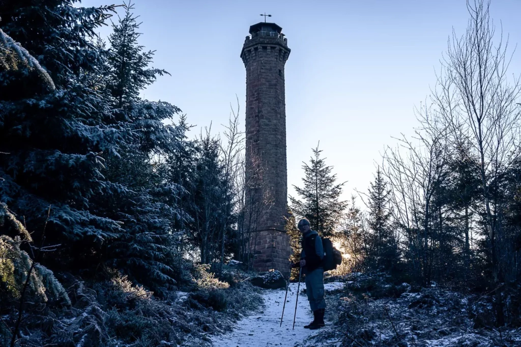 Wanderer steht vor hohem Steinturm im Wald